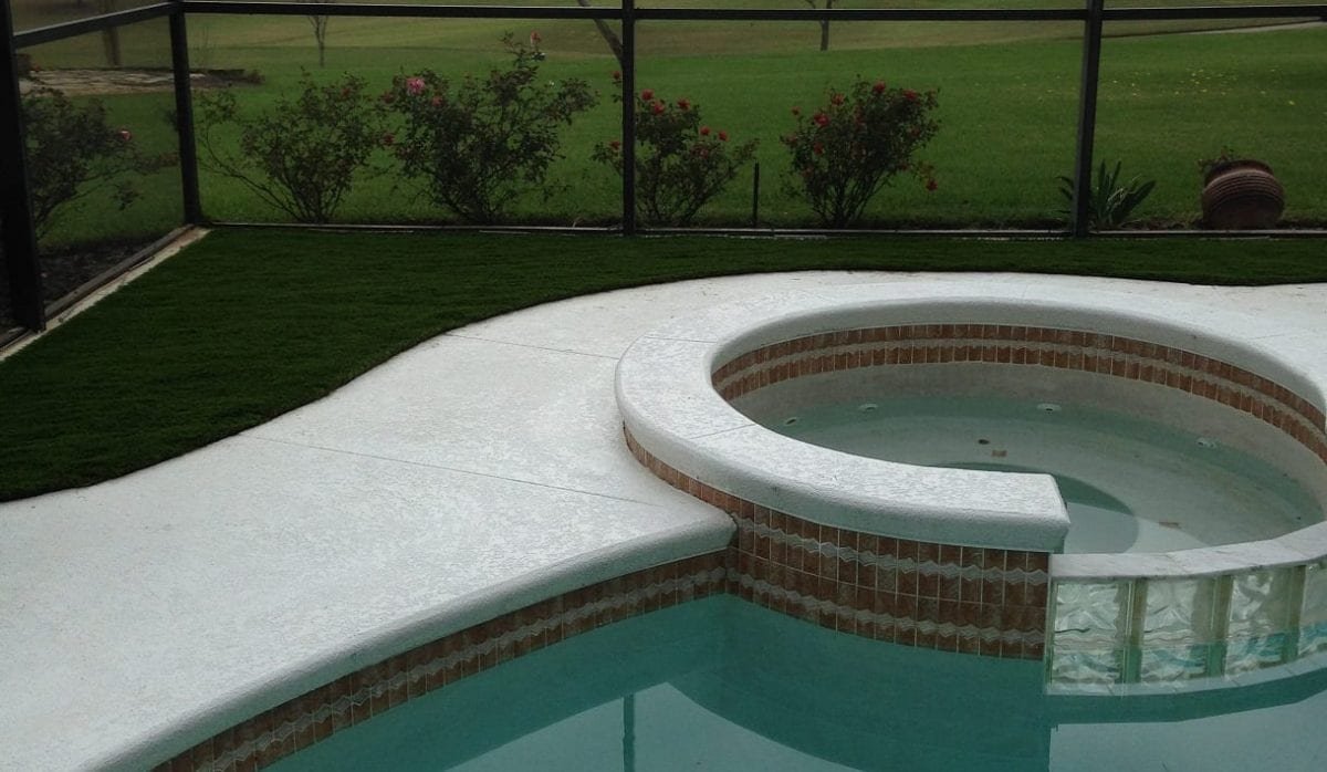 A pool with an attached hot tub surrounded by grass and bushes.