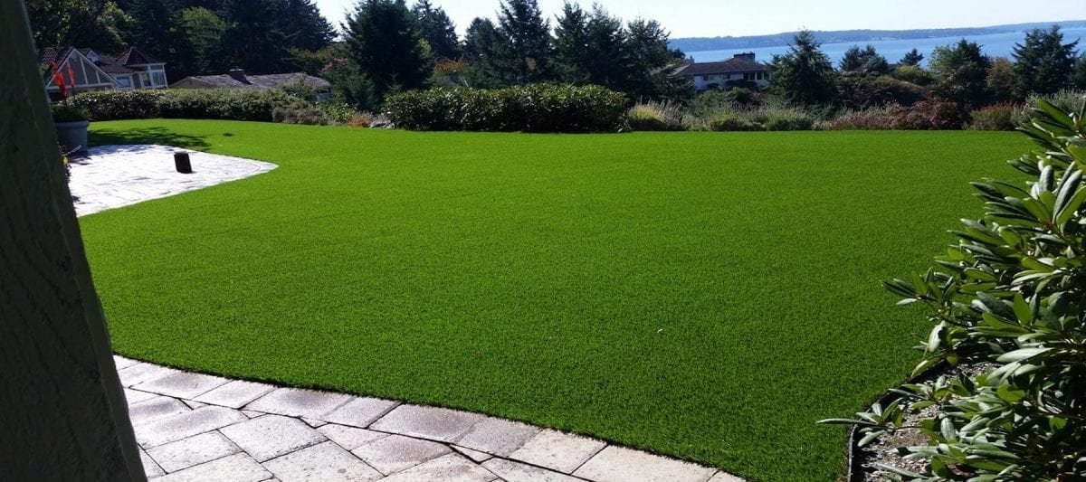 A vibrant green artificial turf lawn with a stone patio edge.