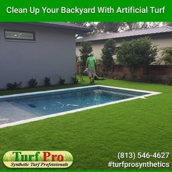 Backyard with artificial turf surrounding a pool and a worker installing it.