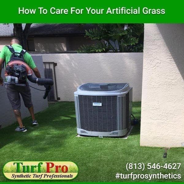 A worker cleans artificial grass near an air conditioning unit.