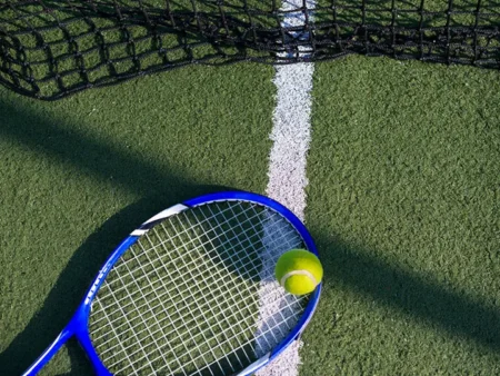 A tennis racket and ball on a court near the net and baseline.