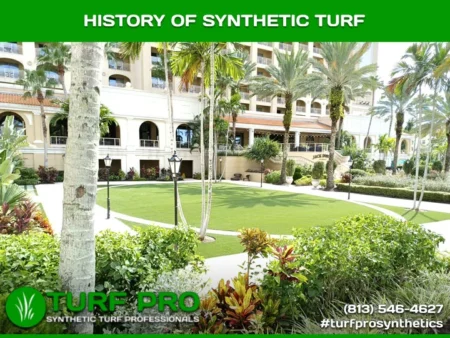 A lush green synthetic turf area surrounded by tropical plants and a building.