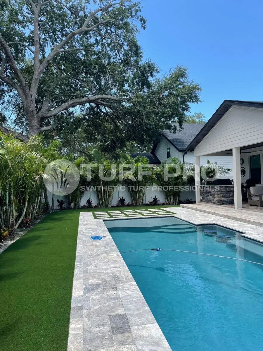 Backyard pool with synthetic turf and trees.