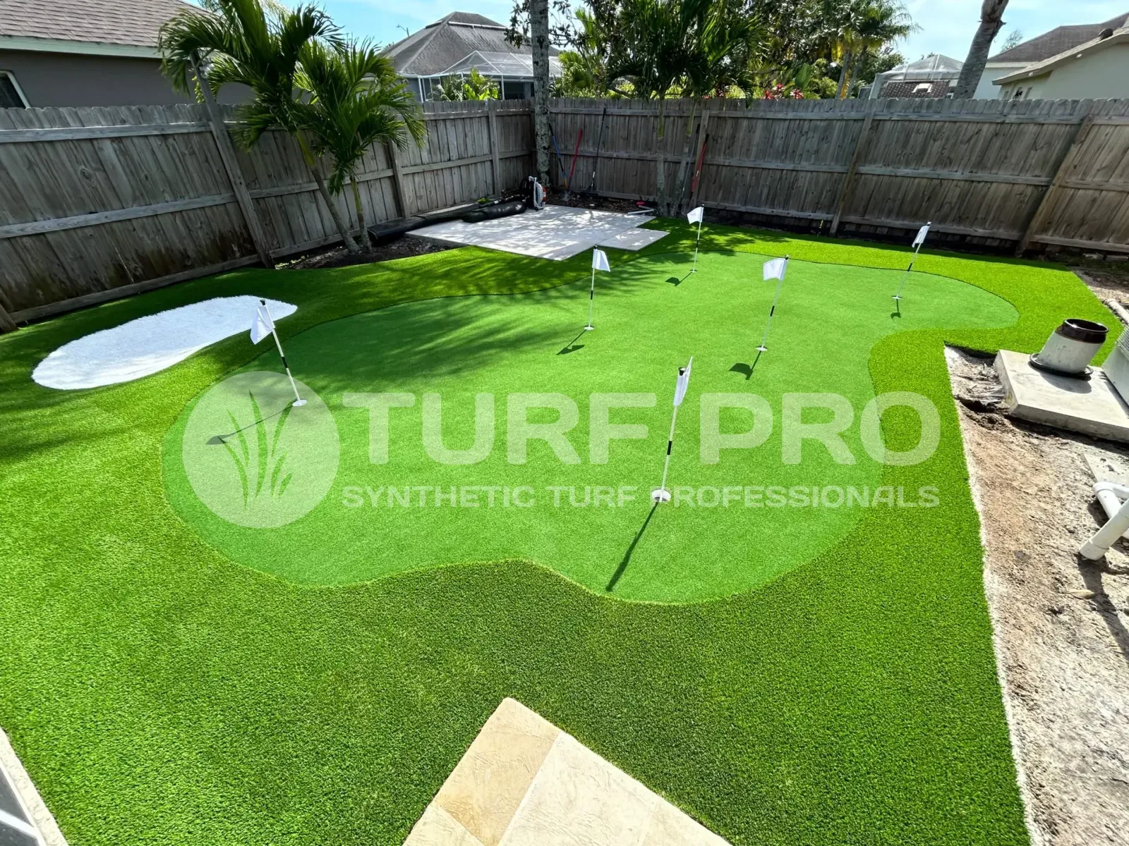 A backyard with pristine synthetic turf and a few palm trees under a clear sky.
